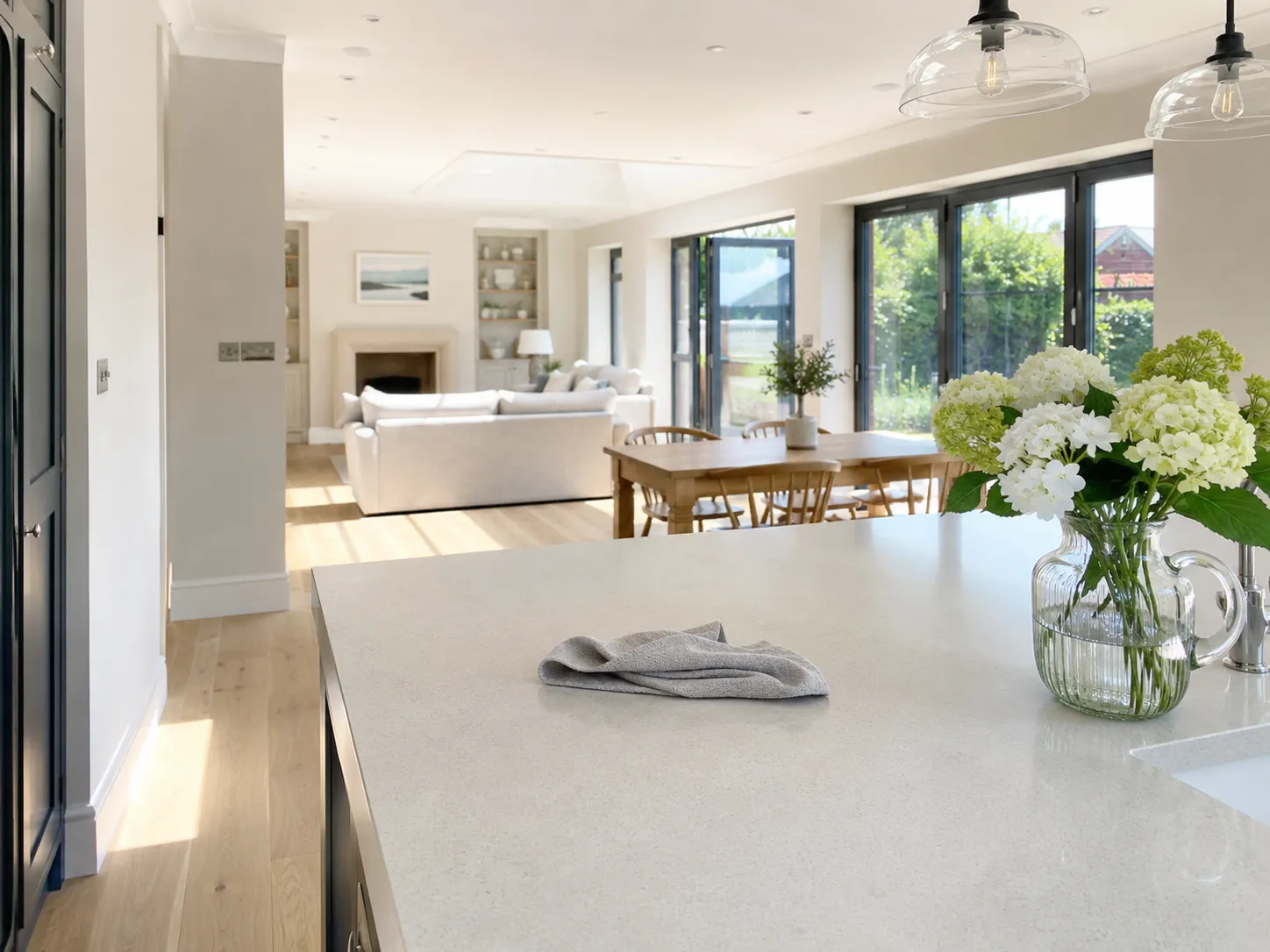 Sunlit open-plan kitchen with a microfibre cloth on the quartz island worktop and fresh hydrangeas in a glass jug