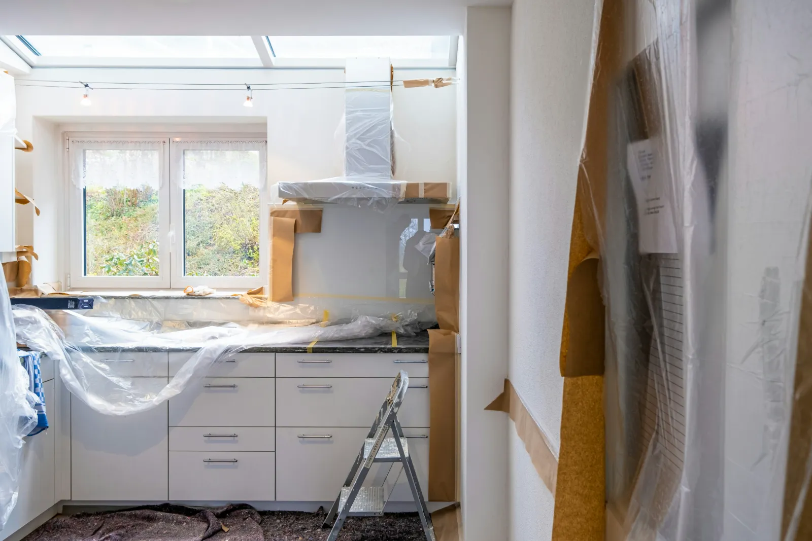 Kitchen mid-renovation with cabinets under dust sheets, masking paper and a step ladder, awaiting an after-builders clean